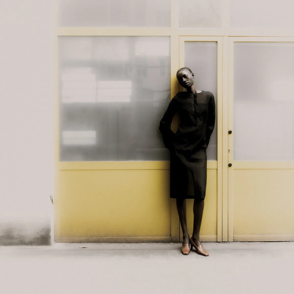 A figure dressed in black beside a yellow door with frosted glass.